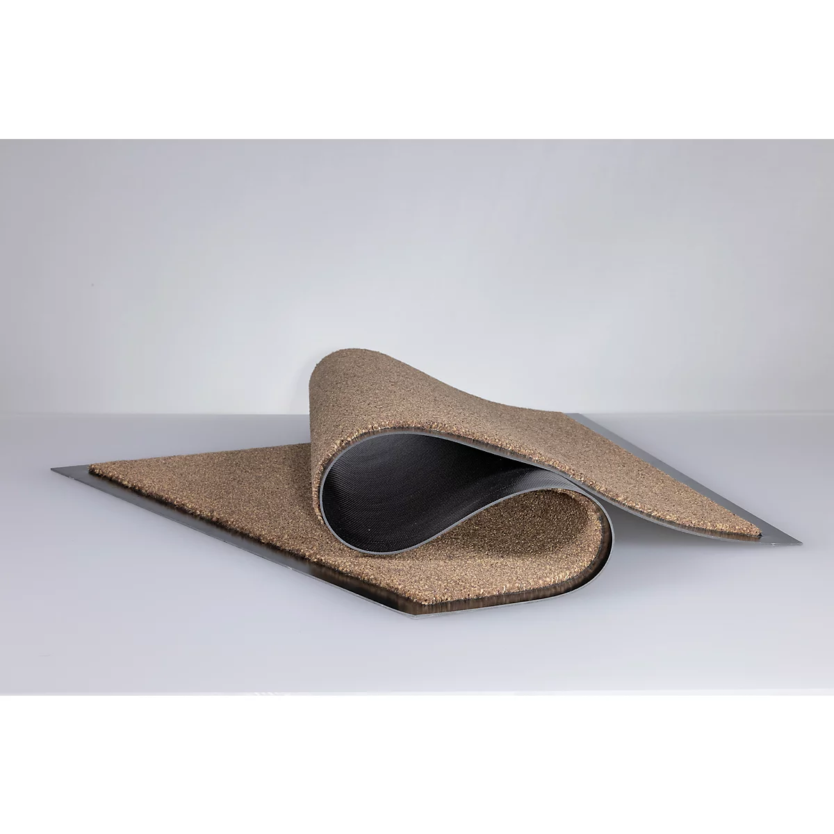 Un paillasson flexible et brunâtre à la texture grossière est plié vers le haut au centre.