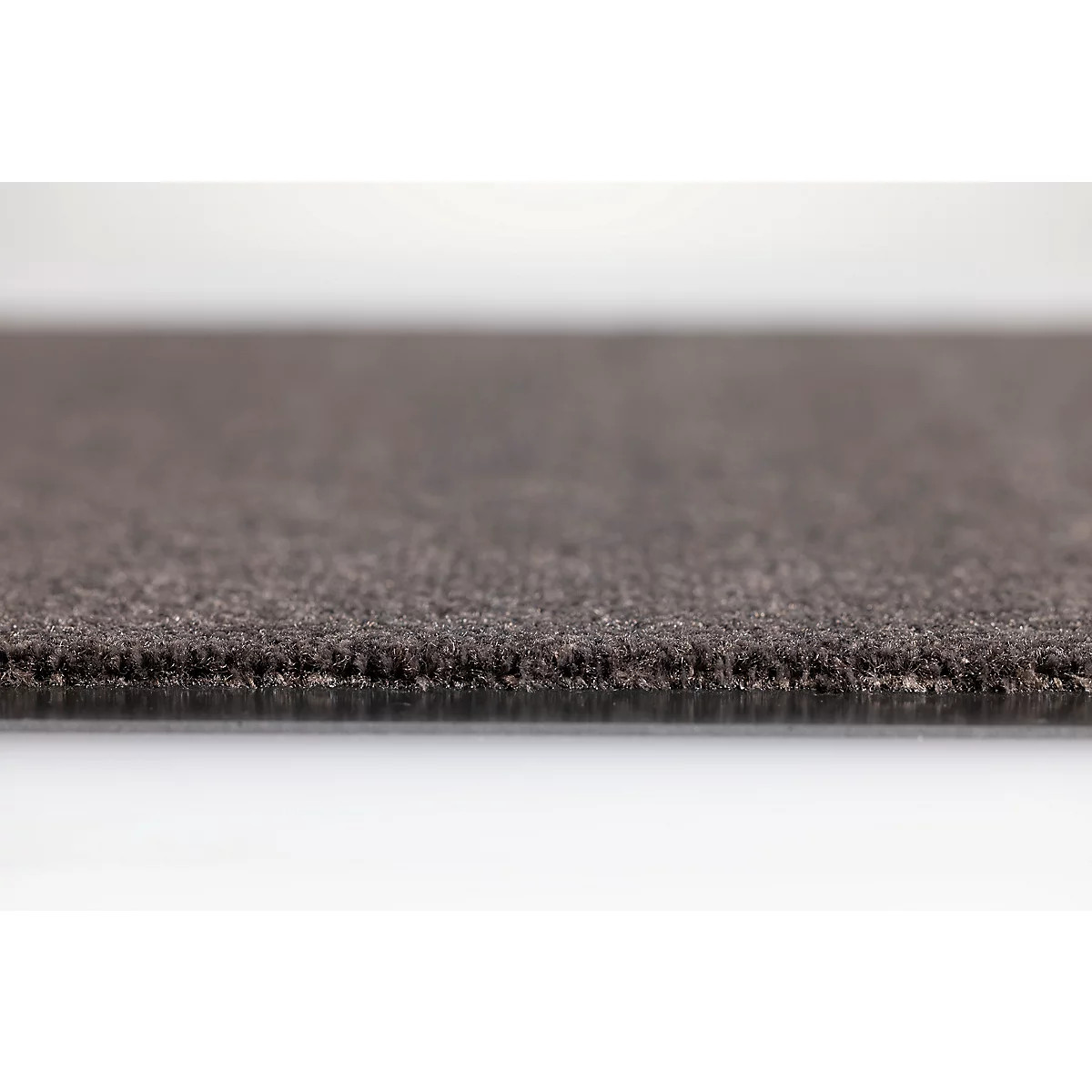 Gros plan sur le bord d'un tapis foncé à la surface texturée sur un fond clair.