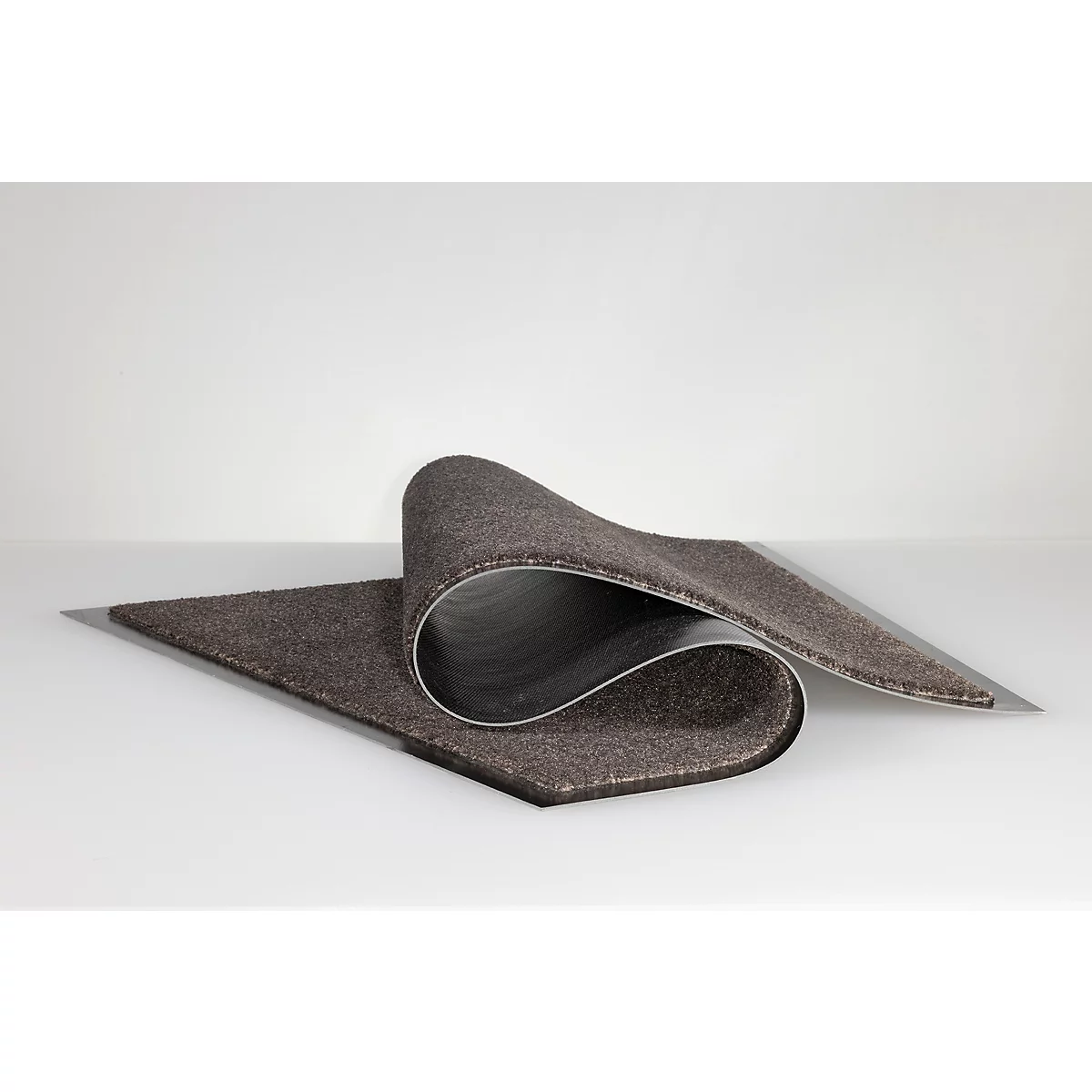 Un revêtement de sol en dalles de moquette marron foncé est présenté légèrement enroulé sur une surface blanche.