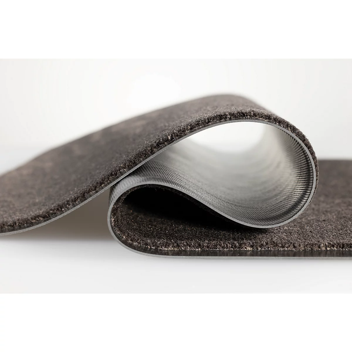 Un tapis gris et flexible est légèrement enroulé pour montrer la structure de son envers.