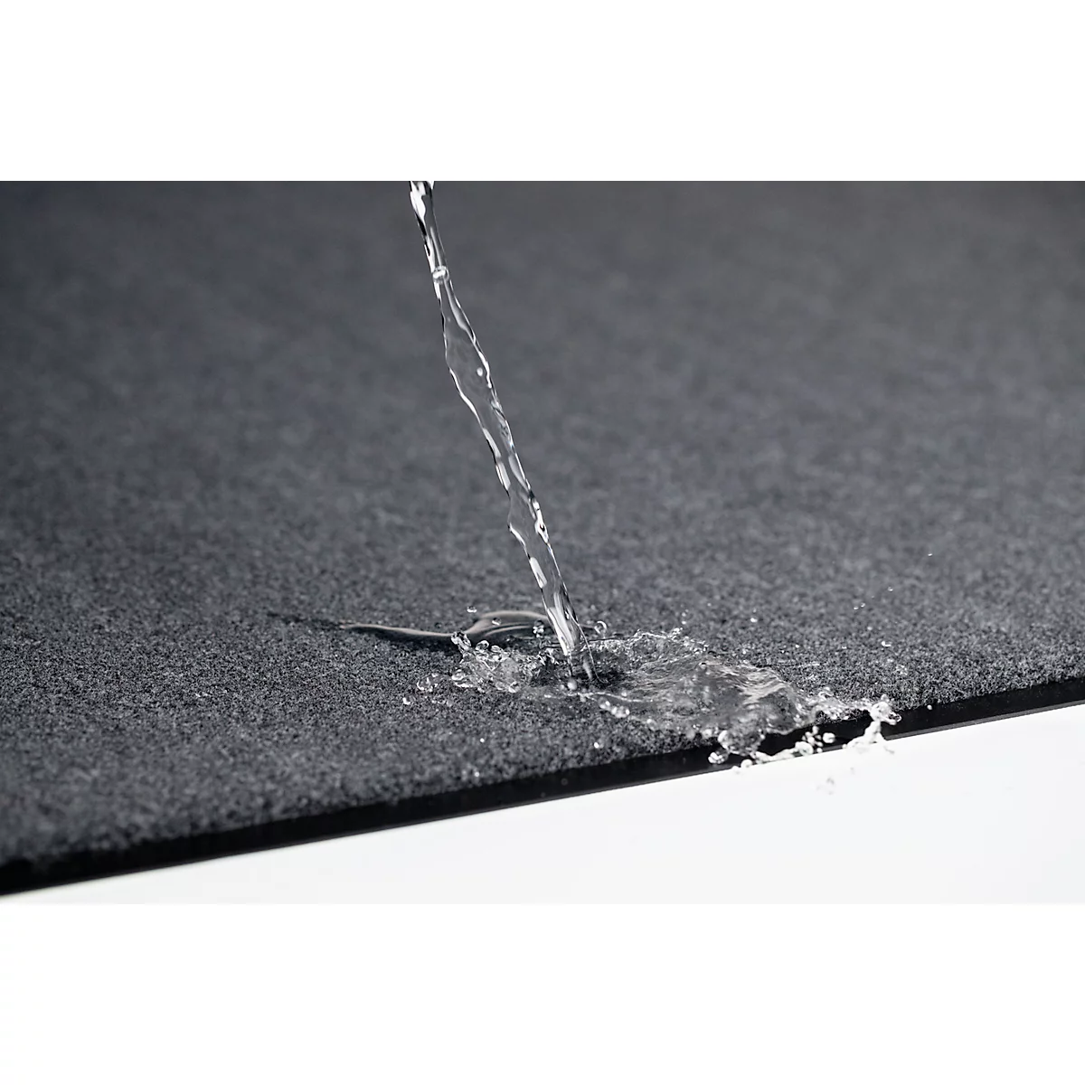 De l'eau est versée sur un tissu noir texturé. Le tissu repousse l'eau. Le fond est blanc.