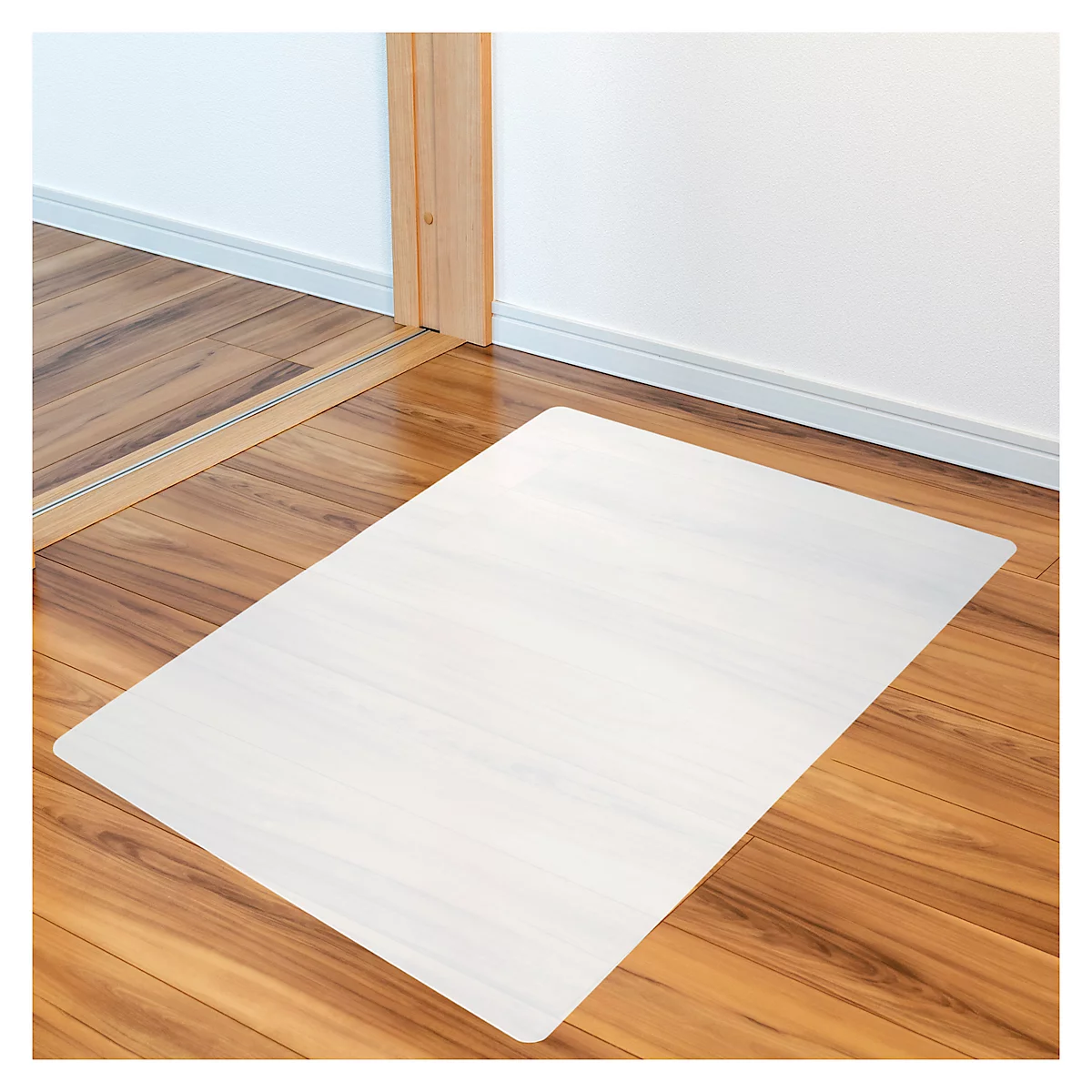 Tapis de sol transparent rectangulaire sur parquet. L'arrière-plan est un mur blanc et un cadre de porte en bois.