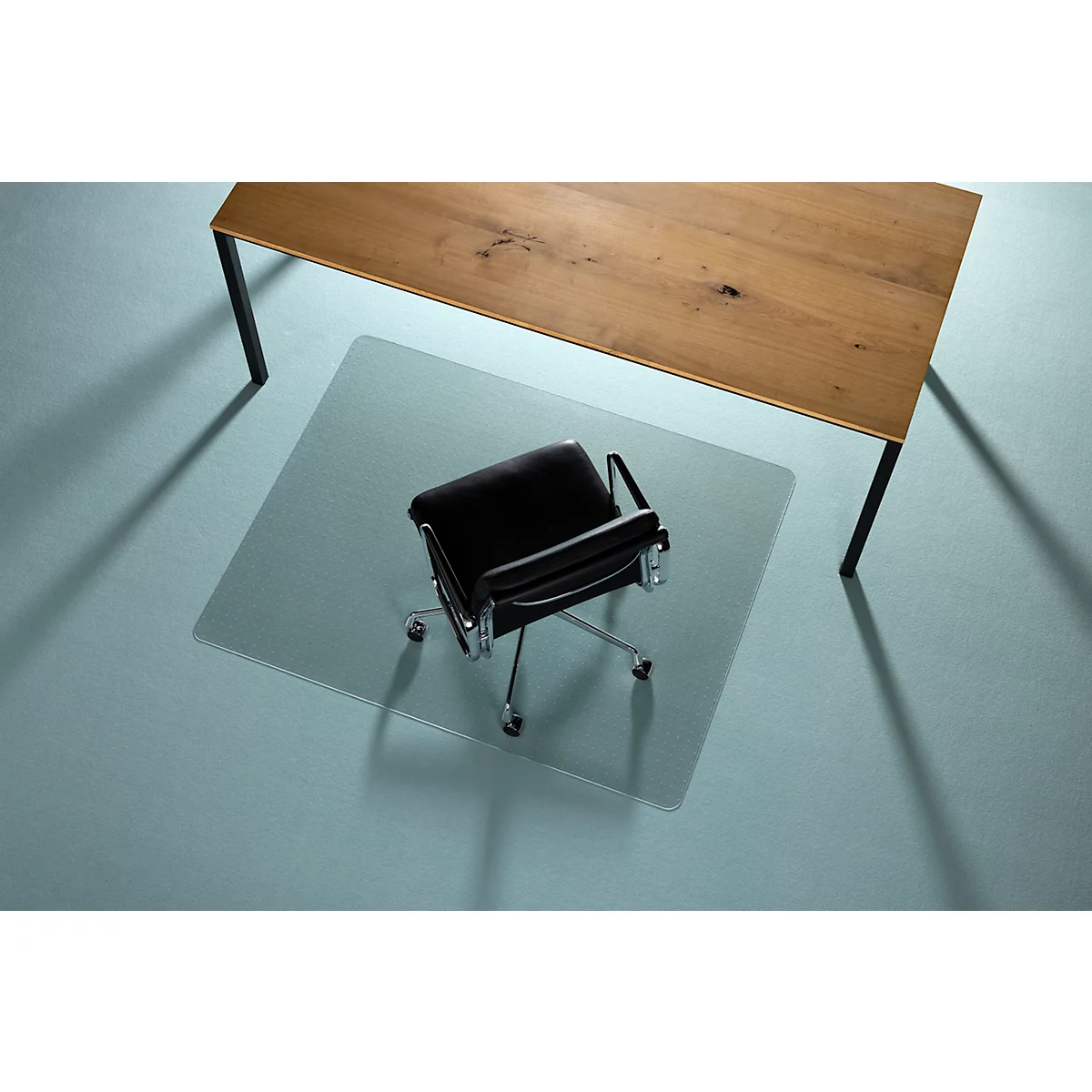 Chaise de bureau sur tapis de protection de sol transparent sous une table en bois. Carrelage bleu.