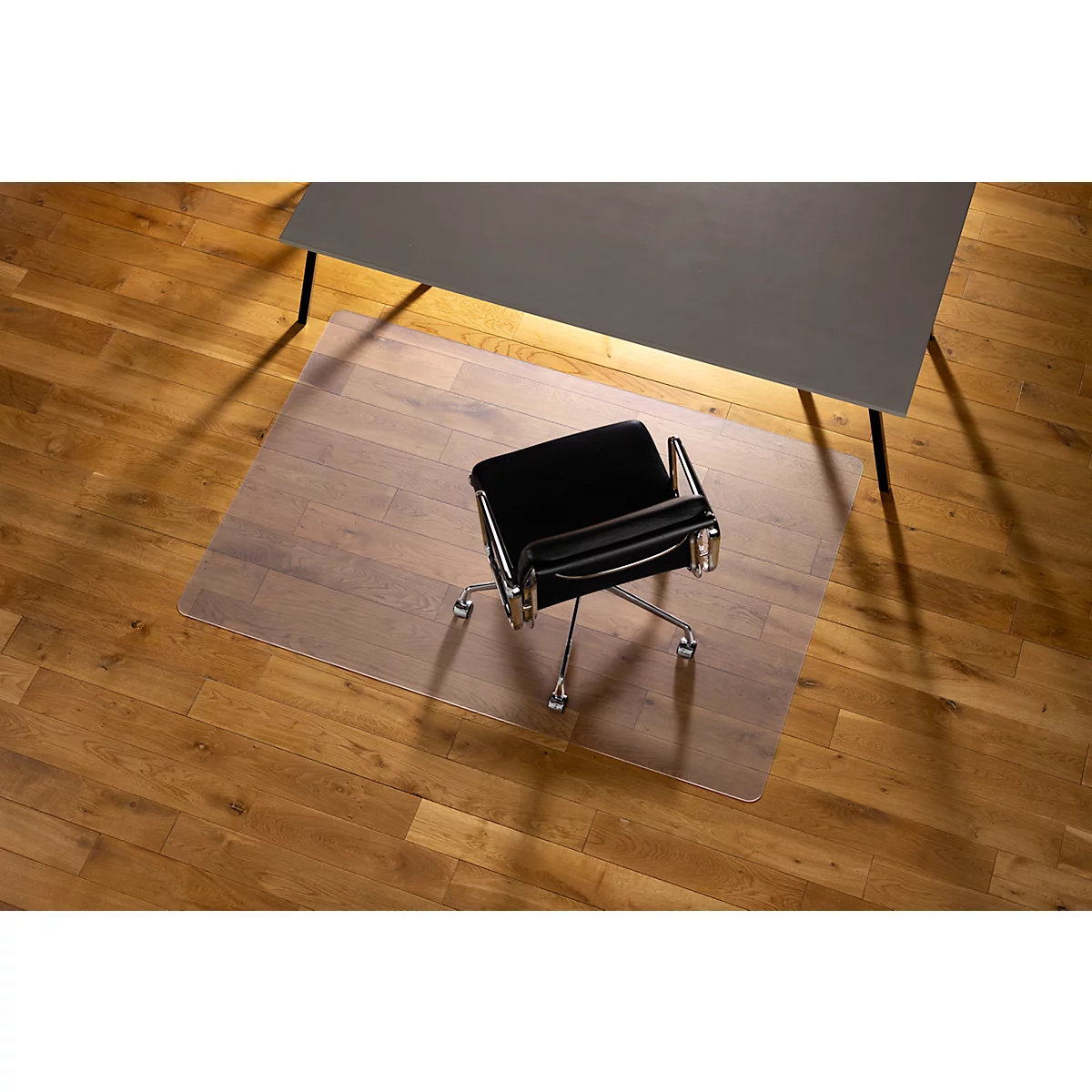 Une chaise de bureau est posée sur un tapis de protection de sol transparent sous un bureau gris.
