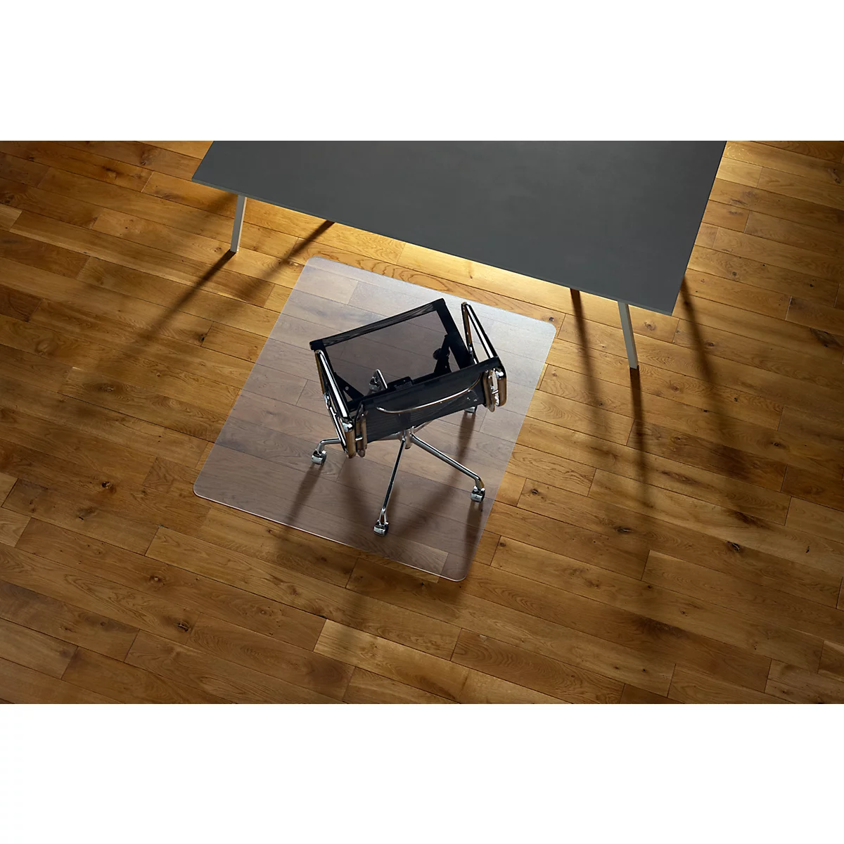 Chaise de bureau sur un tapis de sol transparent devant un bureau sombre. Le sol est en bois.