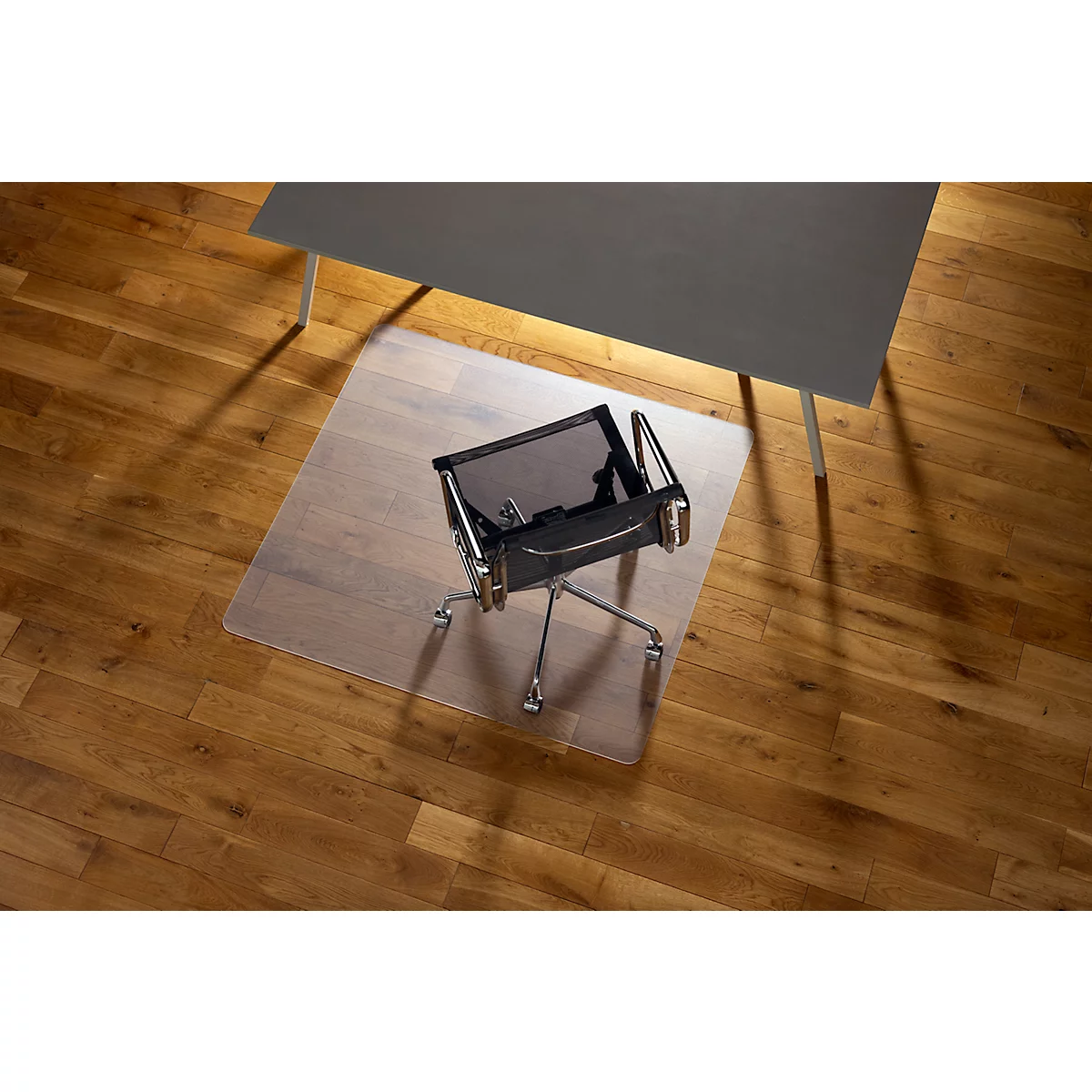 Chaise de bureau sur tapis de protection transparent sous un bureau gris.
