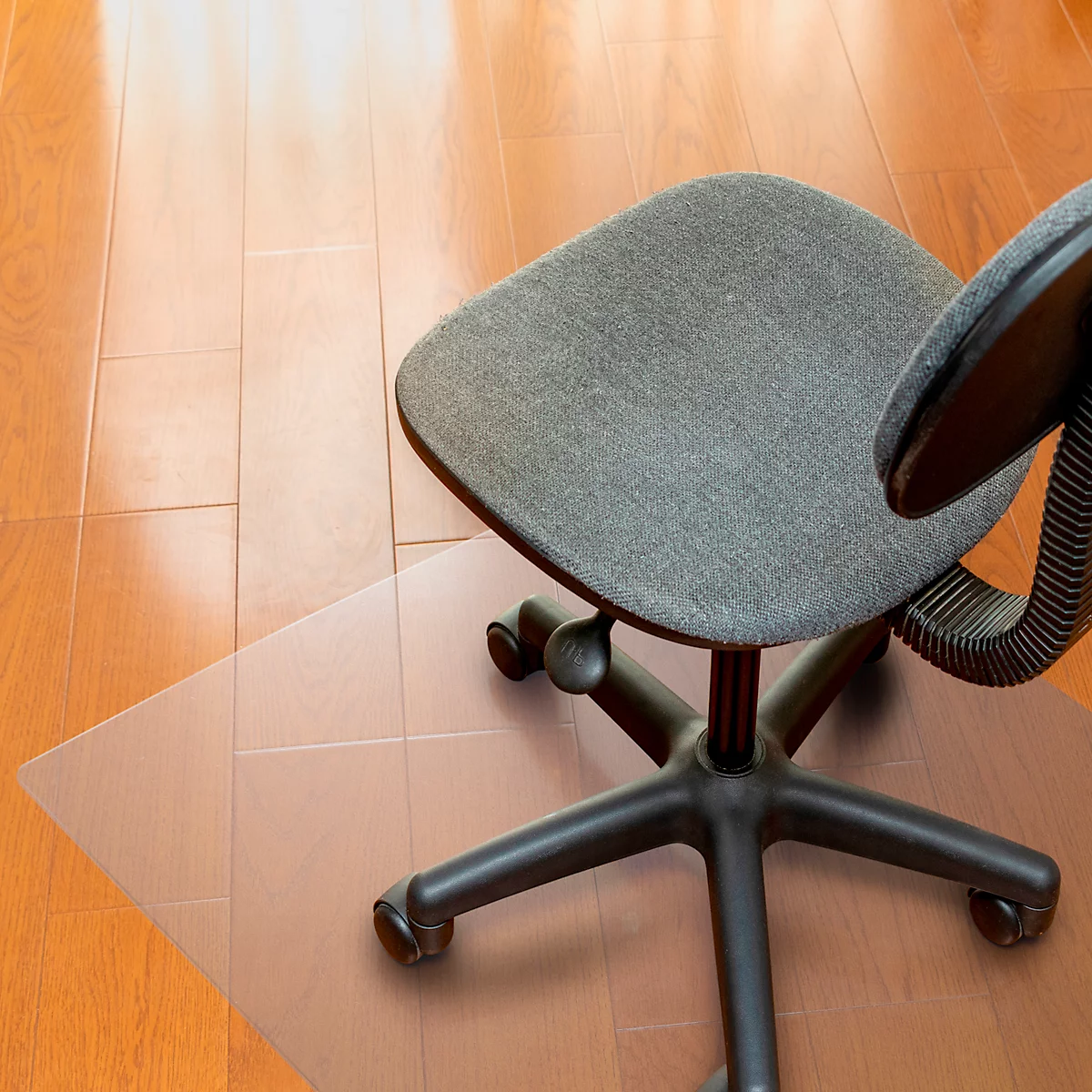 Un fauteuil de bureau gris est posé sur un protecteur de sol transparent, lui-même posé sur un plancher en bois.