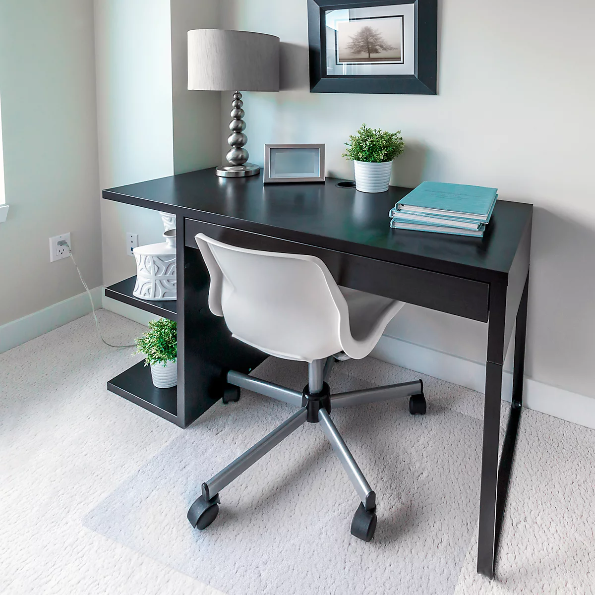Bureau avec chaise de bureau et lampe. Des livres et une plante en pot sont sur le bureau. Une image est accrochée en arrière-plan.