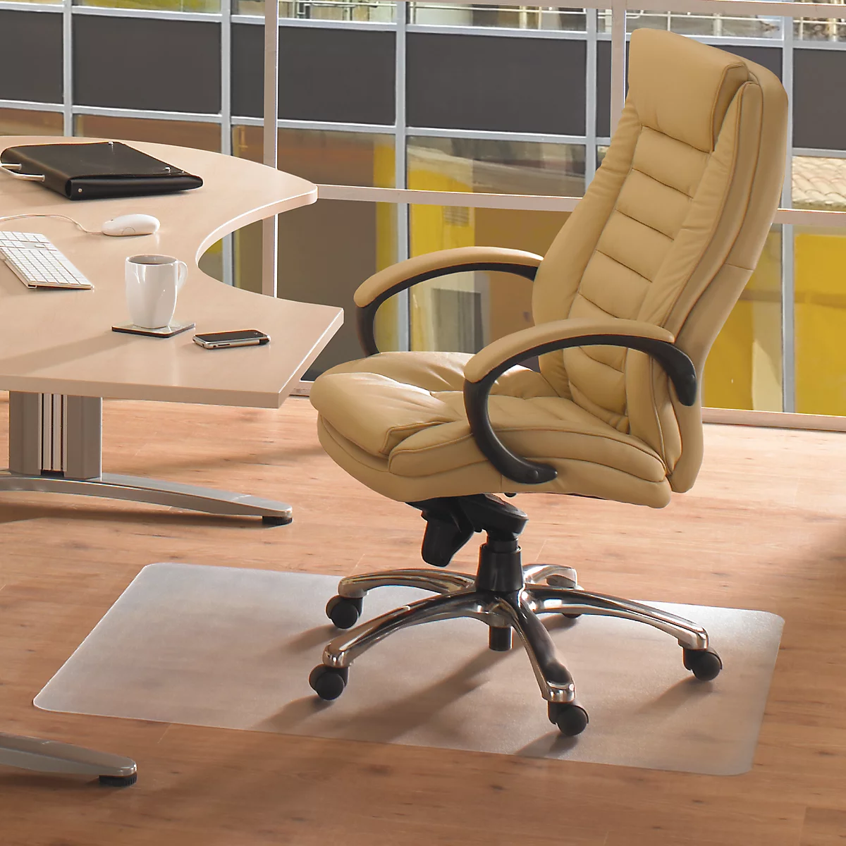 Chaise de bureau et table avec accessoires sur plancher en bois clair. Un tapis de protection transparent est devant la chaise.