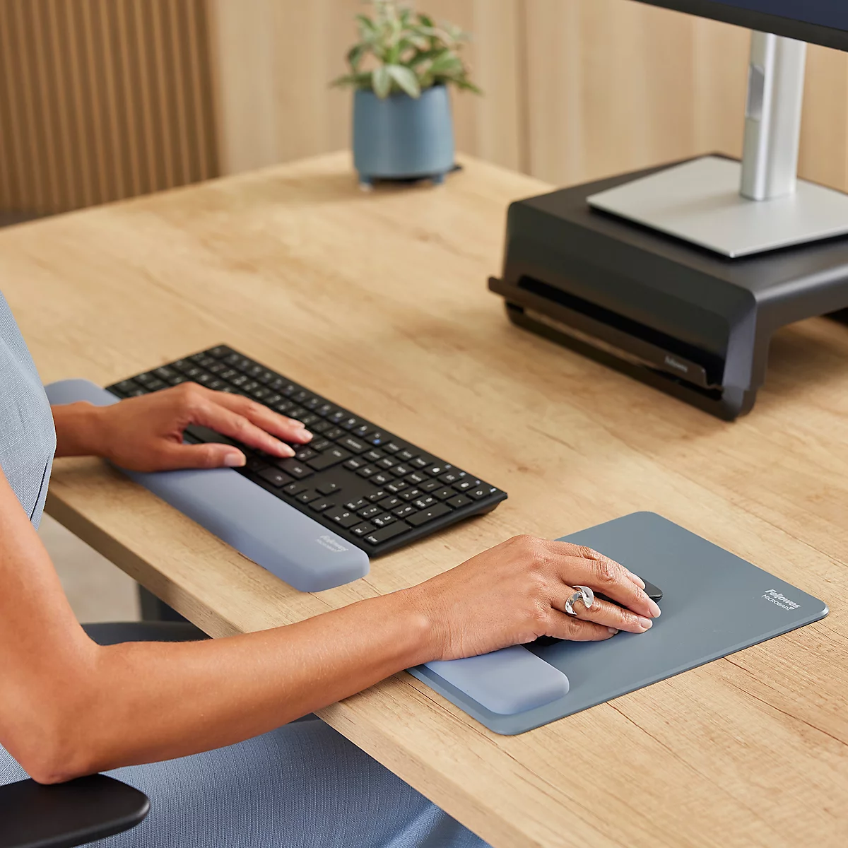 Gros plan d'une personne travaillant à un bureau avec un clavier et une souris. Des repose-poignets sont visibles.