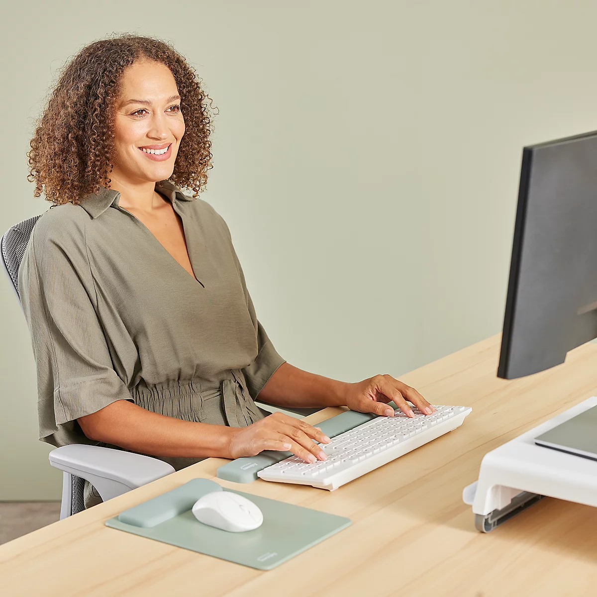 Personne tapant sur un clavier blanc. Souris, tapis de souris et repose-poignet verts. Bureau en bois.