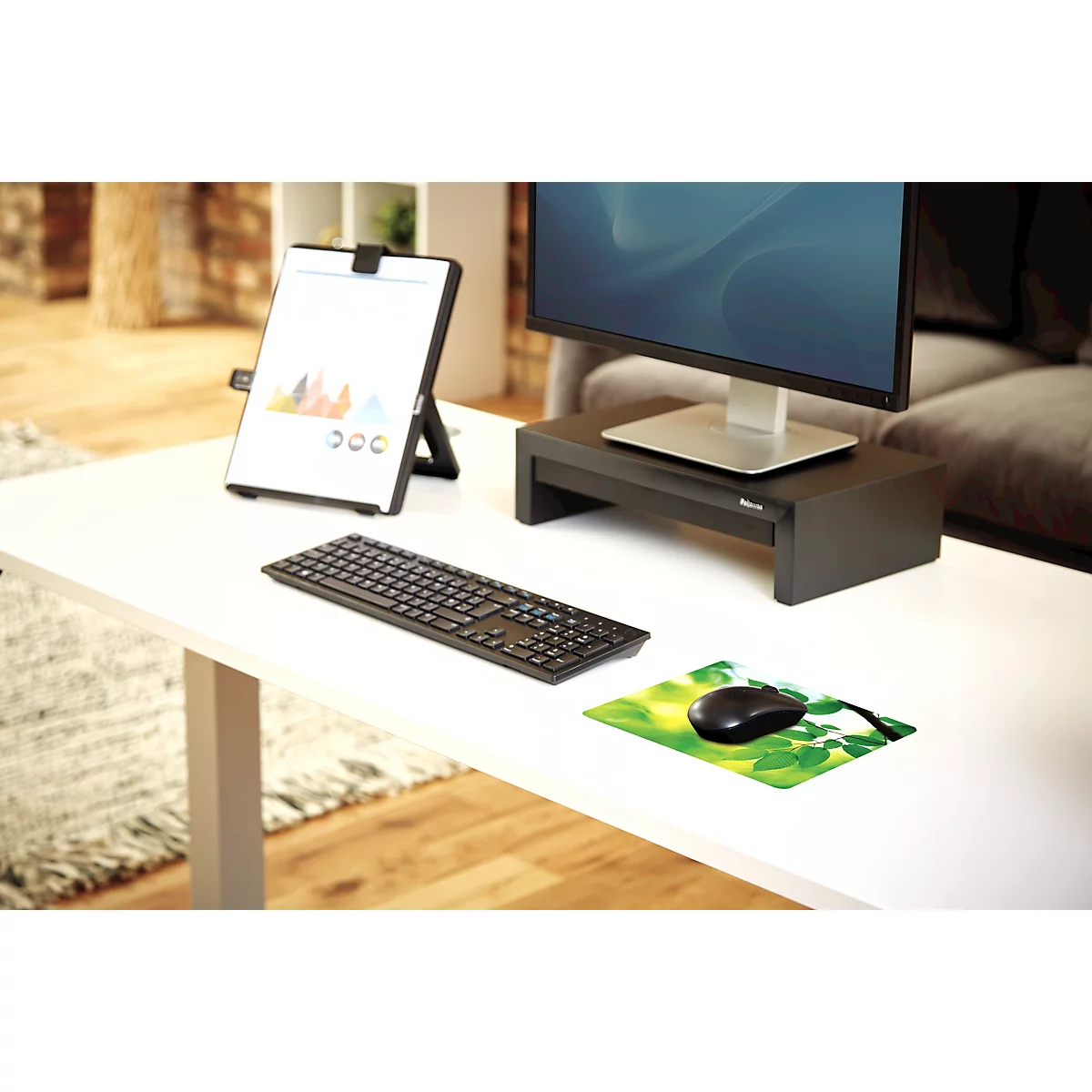 Une main repose sur une souris, qui est sur un tapis de souris avec des feuilles et des couleurs vertes.