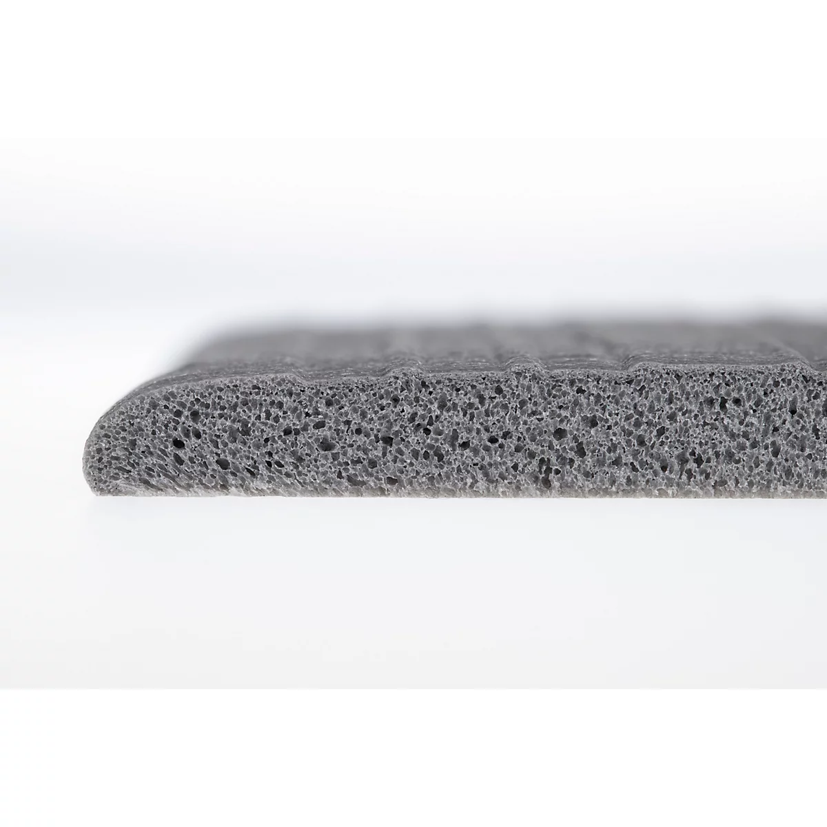 Vue latérale d'un bord en mousse gris et poreux avec une forme biseautée sur un fond blanc.