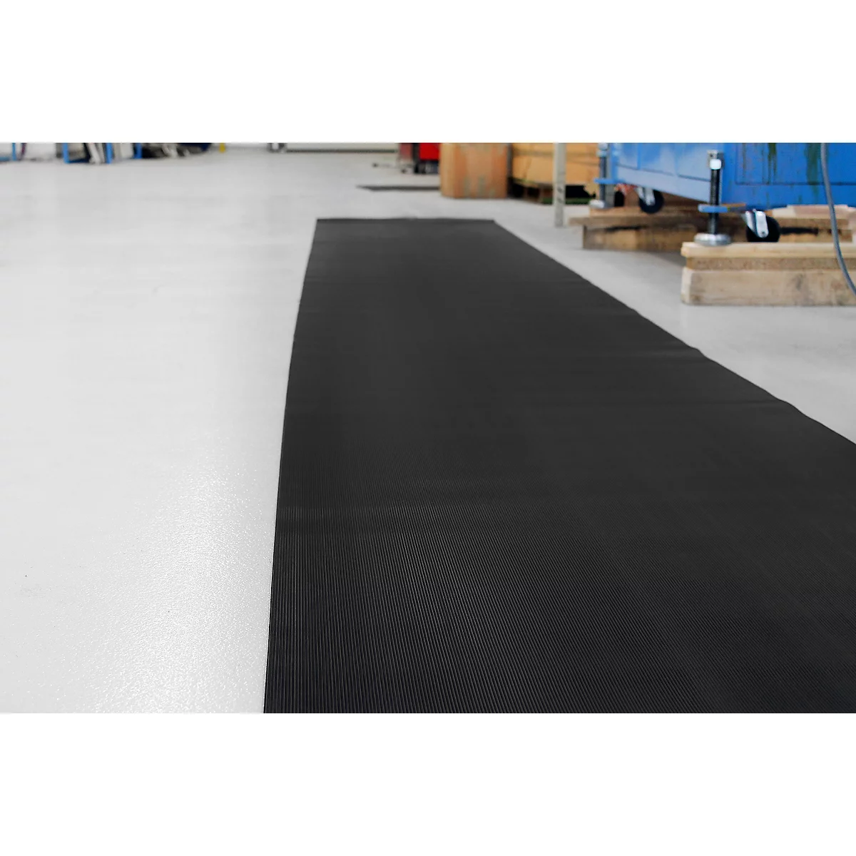 Tapis en caoutchouc noir sur sol industriel clair. Outils et machines en arrière-plan.
