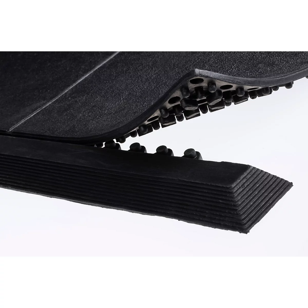 Gros plan d'un tapis en caoutchouc noir avec un dessous à picots et un bord biseauté sur fond blanc.
