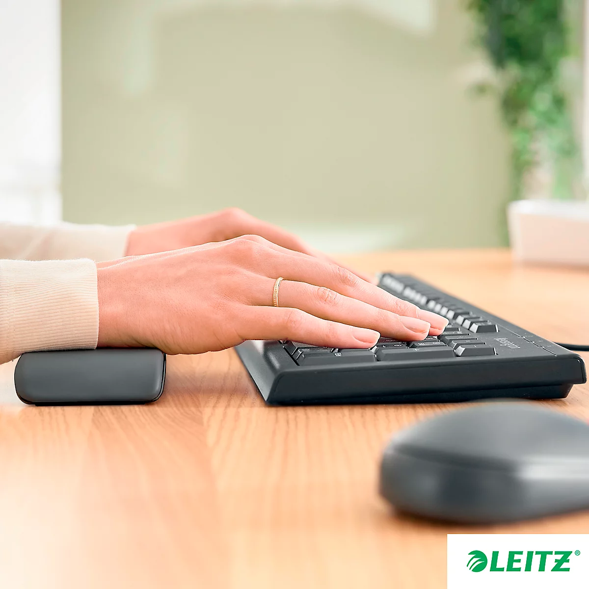 Les mains d'une femme tapant sur un clavier avec un repose-poignet et une souris. Le logo Leitz est visible sur la table.