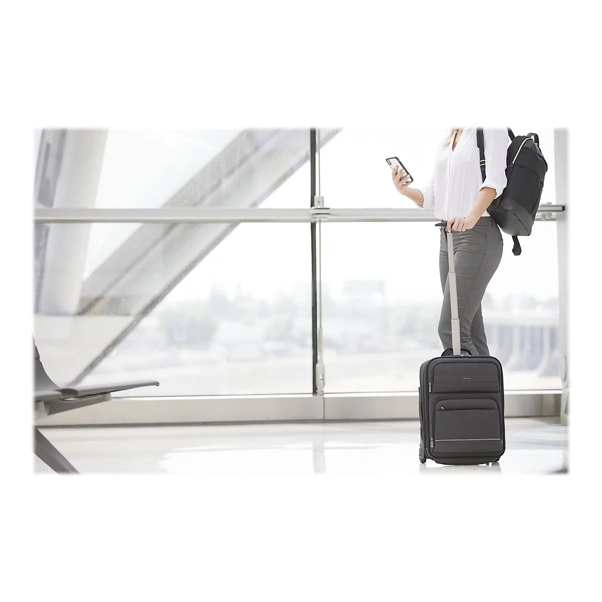 Frau im Flughafen mit Koffer und Smartphone. Sie trÃ¤gt einen Rucksack.