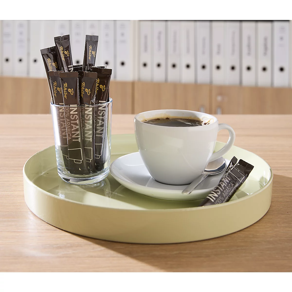 Ein hellgrünes Tablett mit einer Kaffeetasse und einem Glas voller Instant-Kaffeesticks in einem Büro.