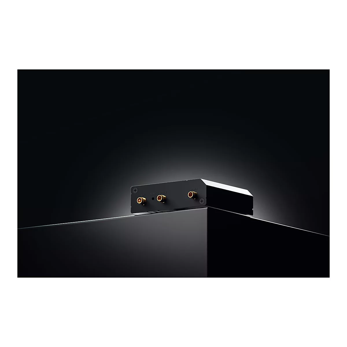 Schwarzes elektronisches Gerät, goldfarbene Anschlüsse. Auf glänzender Oberfläche. Dunkler Hintergrund.