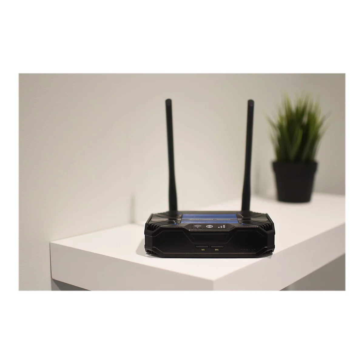 Schwarzer Router mit zwei Antennen. Er steht auf einer weiÃŸen OberflÃ¤che neben einer Topfpflanze.
