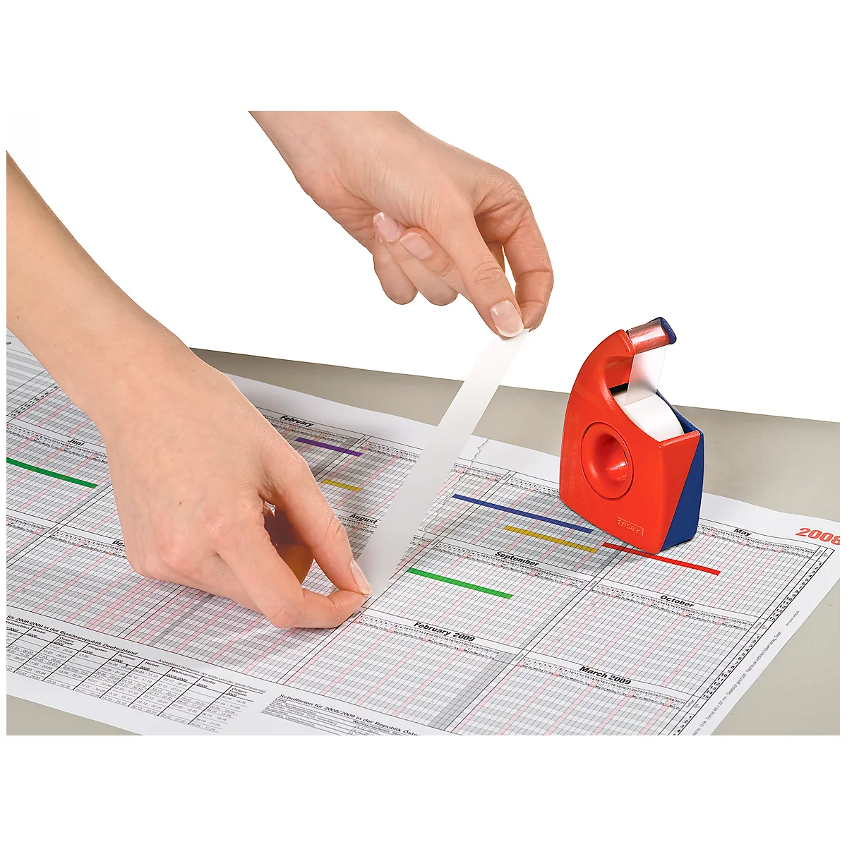 Hands applying tape on a calendar. Red and blue tape dispenser on the right.