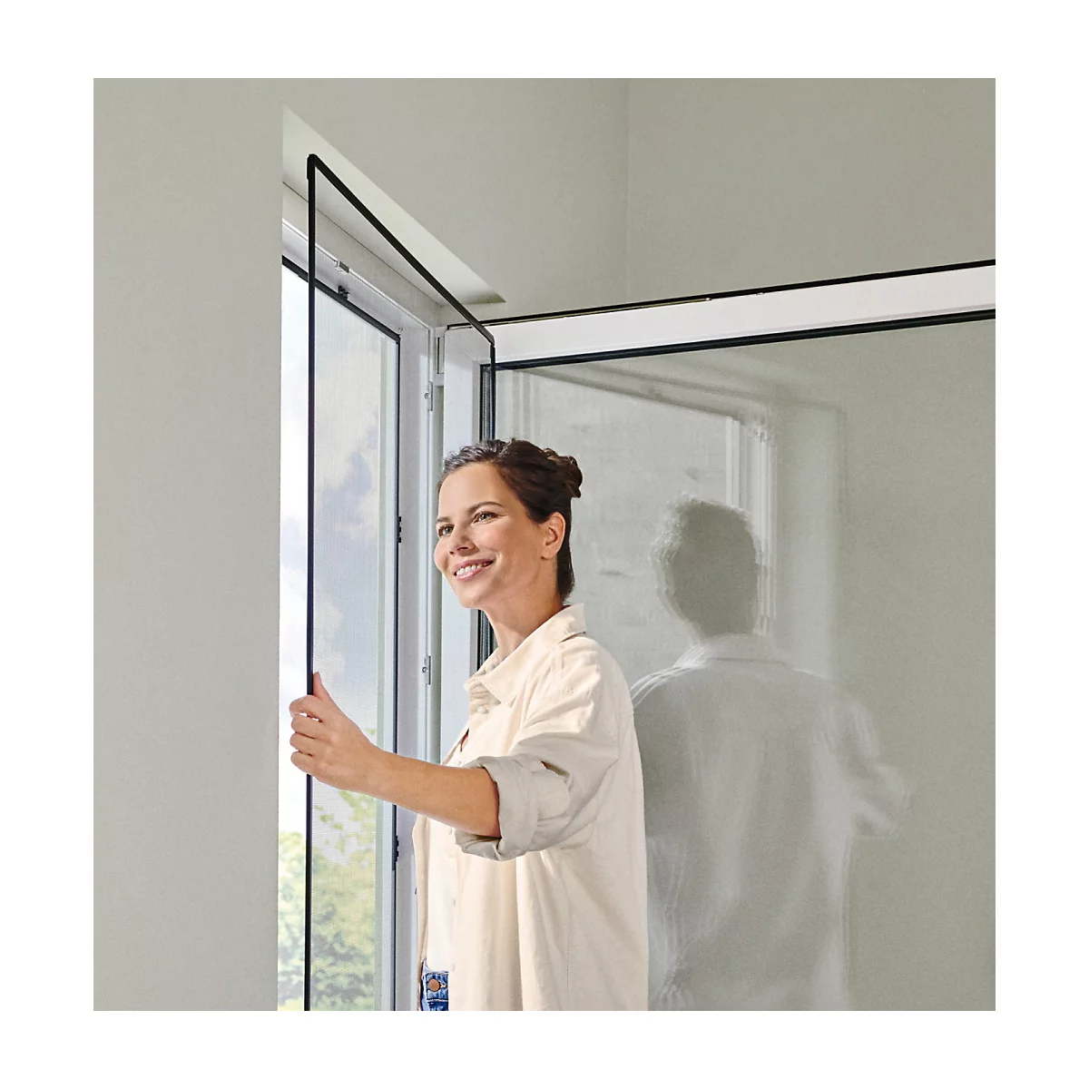 Une femme souriante ouvre une fenêtre avec une moustiquaire.