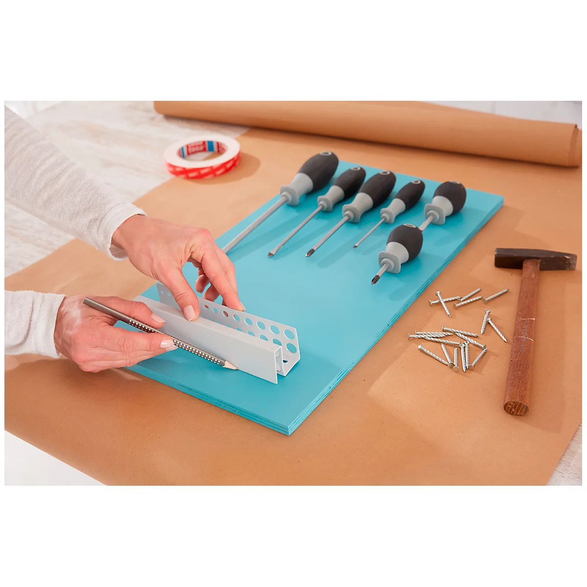 Hands holding angle and pencil on turquoise board with tools. Screwdrivers, hammer and nails are ready.