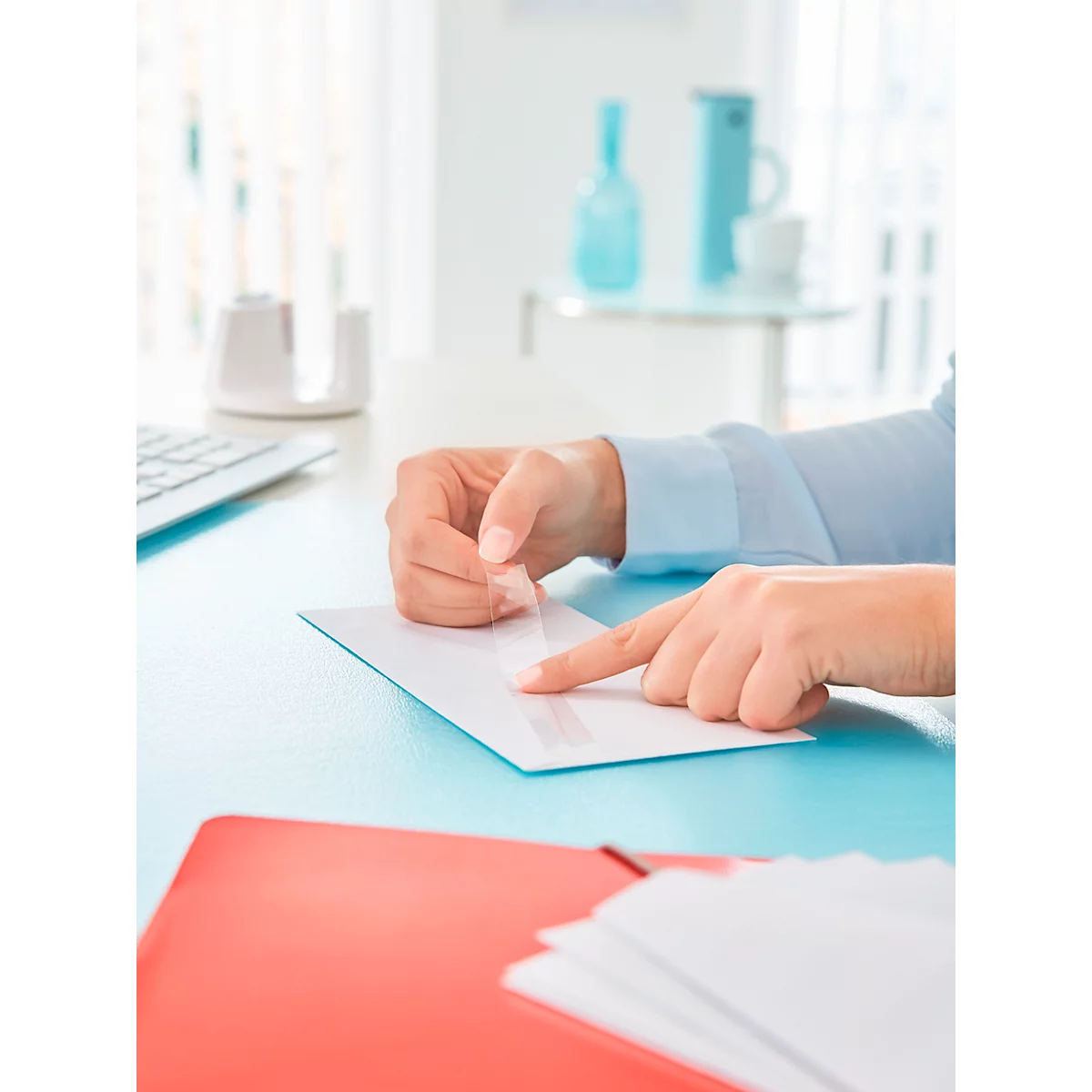 A person is applying adhesive tape to a white envelope. Other letters are lying on a blue table.