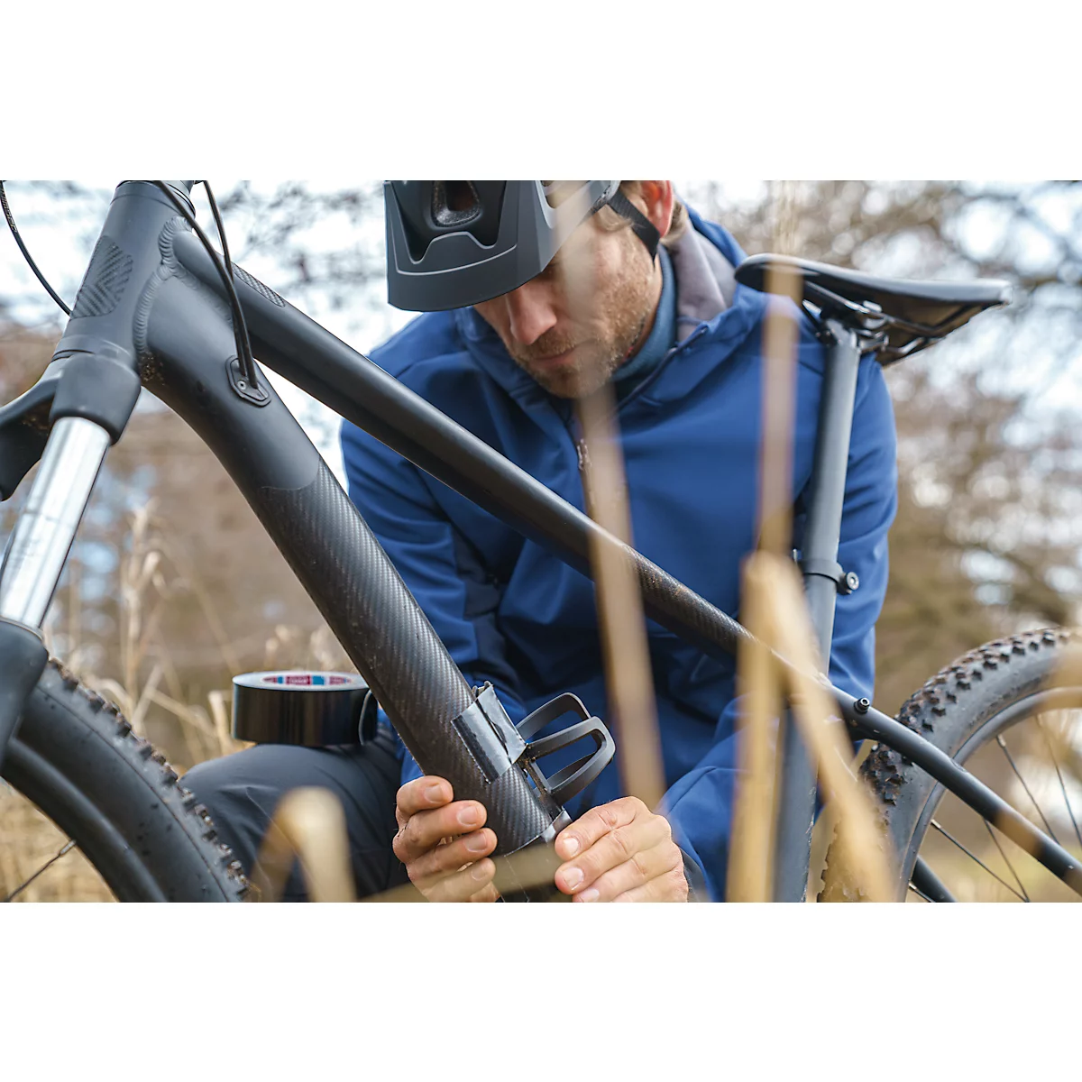 A man repairing a bicycle, he wears a helmet and blue jacket.