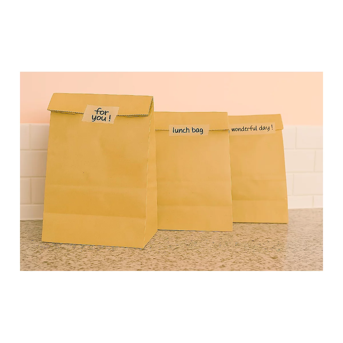 Drei braune Papiertüten mit Aufschriften: "for you!", "lunch bag" und "wonderful day!". Sie stehen auf einer Küchenzeile.