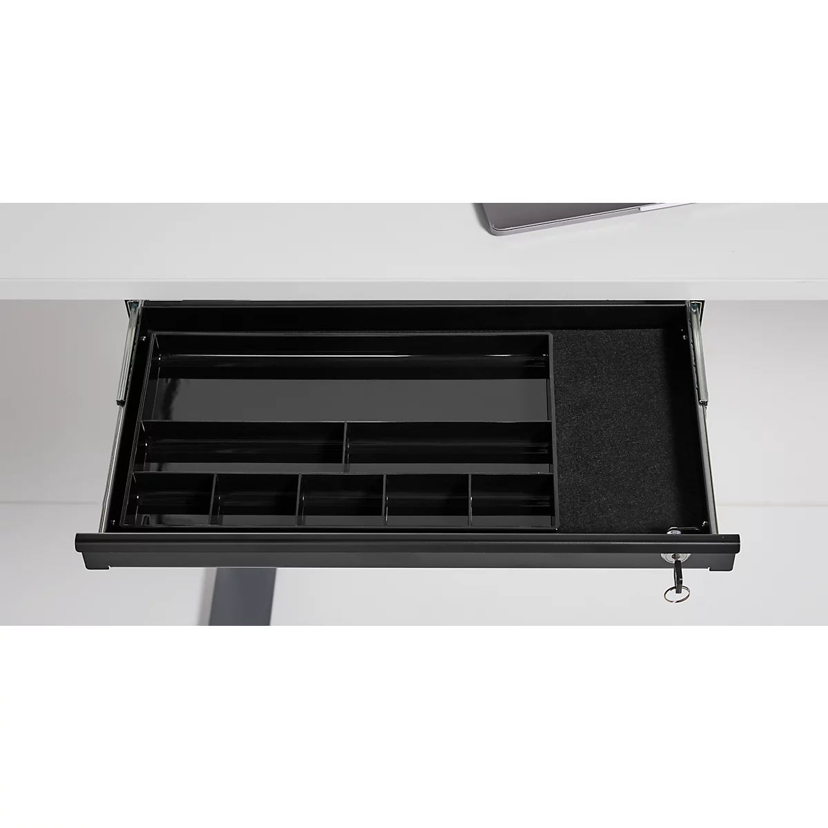 Tiroir de bureau noir sorti, avec divers compartiments pour l'organisation. À l'intérieur : stylos, notes et fournitures.