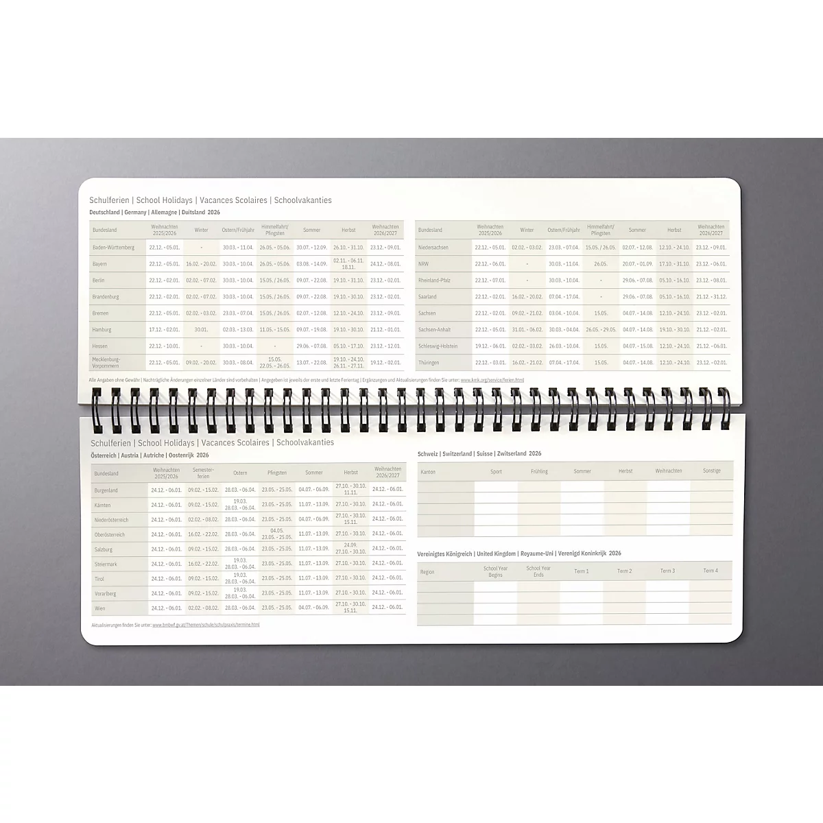 Geöffneter, gebundener Kalender, grauer Hintergrund. Beide Seiten zeigen Tabellen mit Informationen und Uhrzeiten.