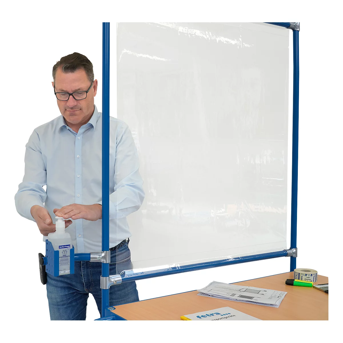 Ein Mann mit Brille an einer Trennwand, benutzt Desinfektionsmittel.