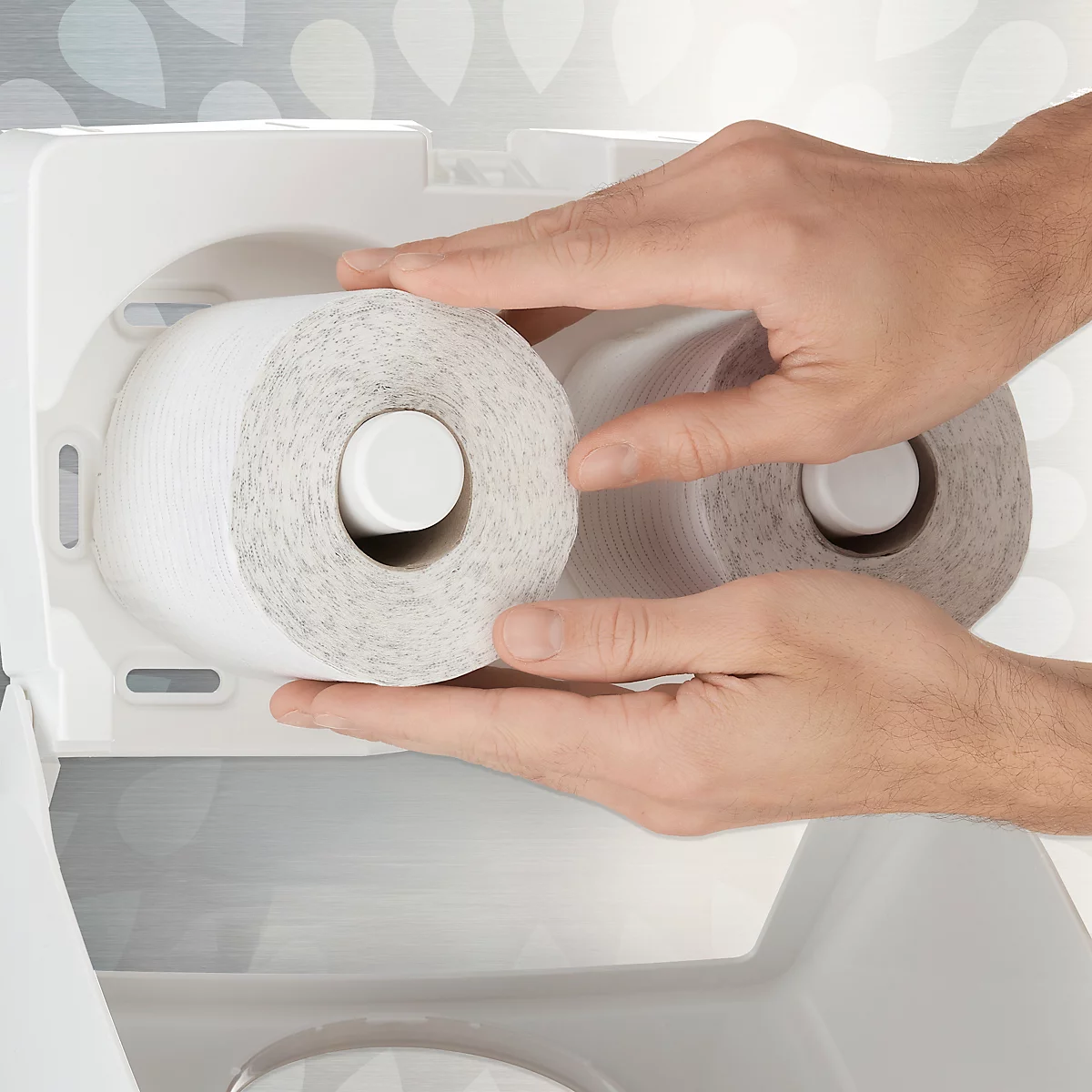 Handen plaatsen toiletpapierrollen in een witte dispenser. Eén rol zit al op zijn plaats.
