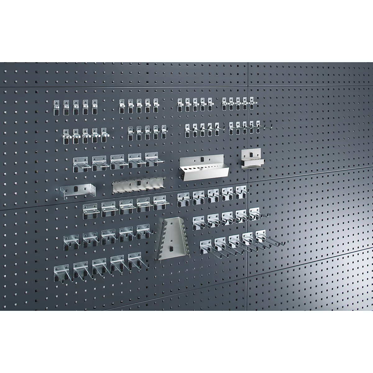 A dark wall displaying various metal tool hangers, arranged in different sizes and shapes.