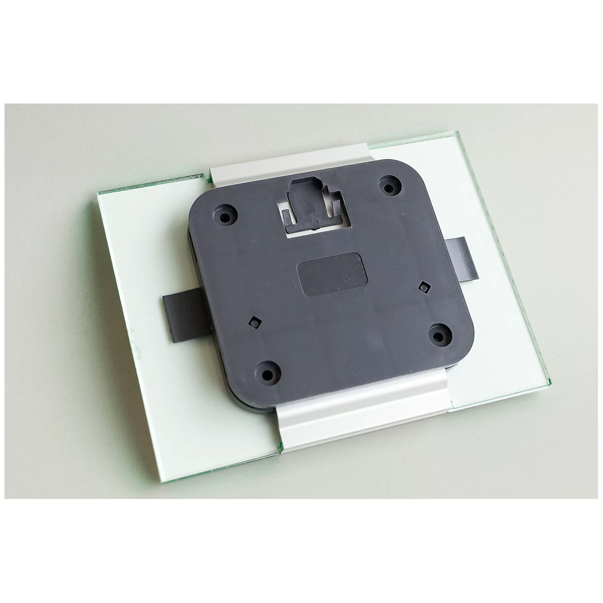 Gray bracket with black plastic plate on glass plate. Holes are attached at the corners.