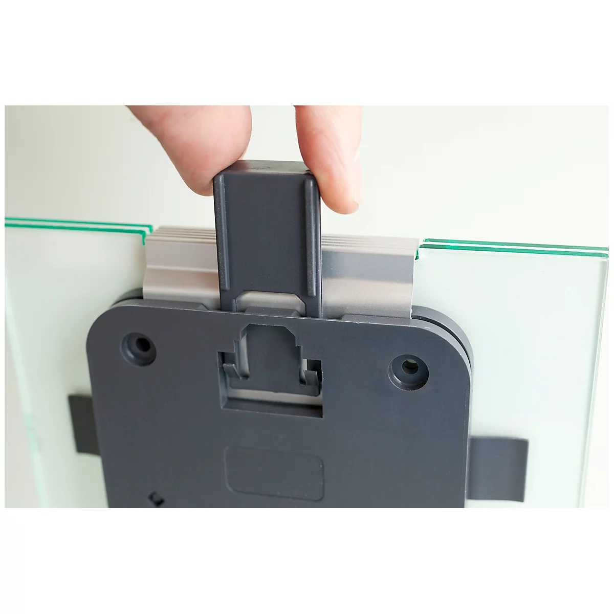 Close-up of a hand attaching a gray plastic closure to a glass picture. In detail, the bracket is being mounted.