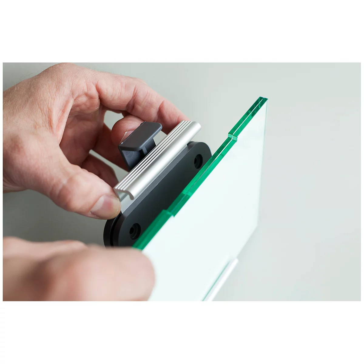 A hand holds a bracket for a glass plate with a green edge. The product is being assembled in the hand.