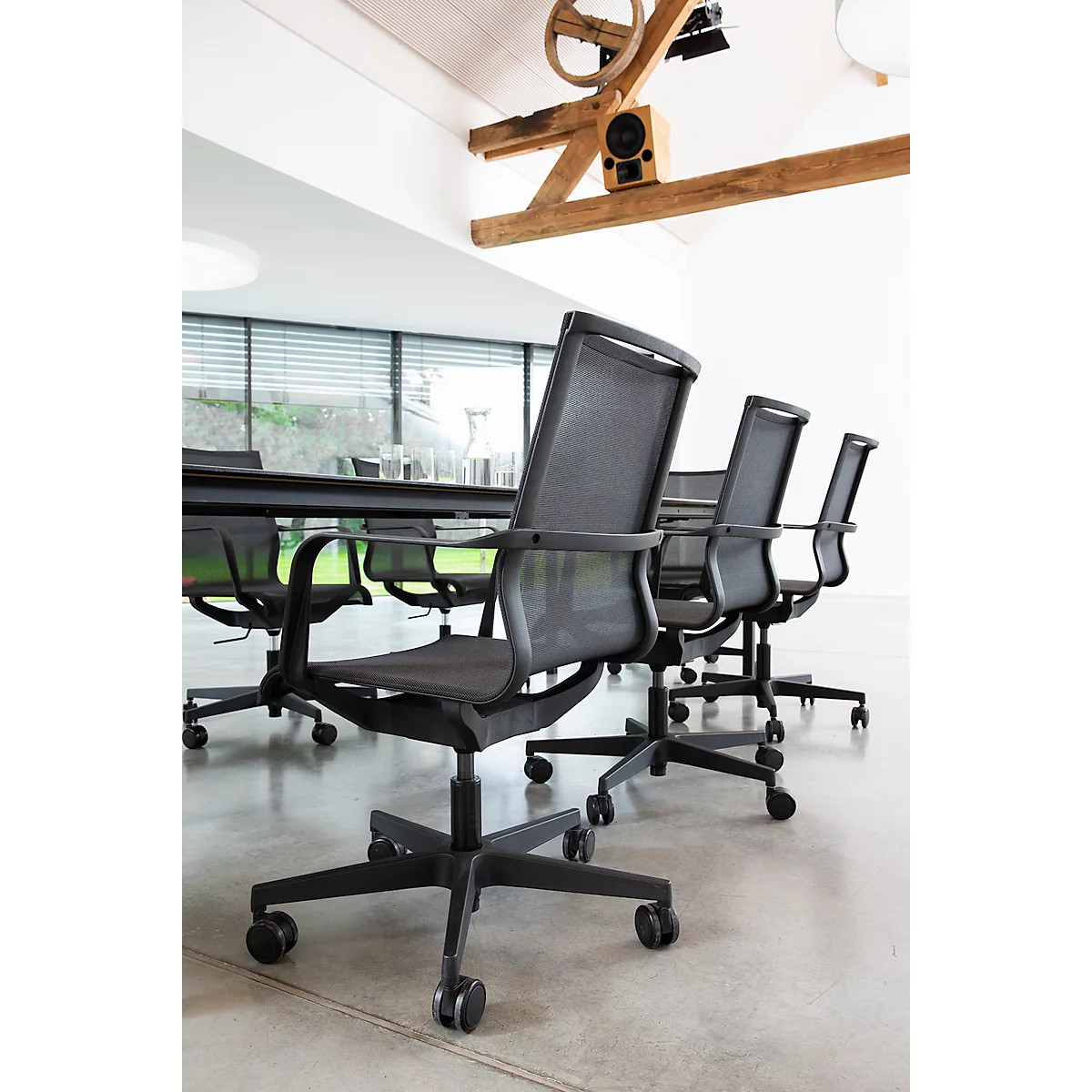 Diverse zwarte bureaustoelen met netbespanning rond een lange vergadertafel in een moderne, lichte kantoorruimte.