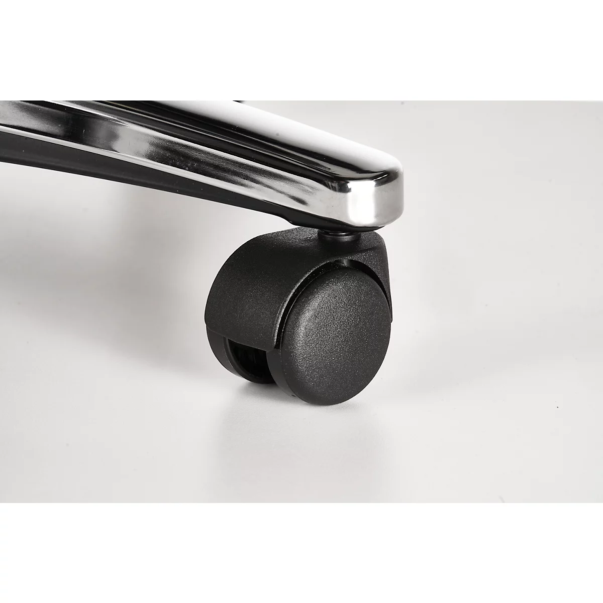 Close-up of an office chair wheel. The wheel is black and placed on a white floor, chrome elements are above.