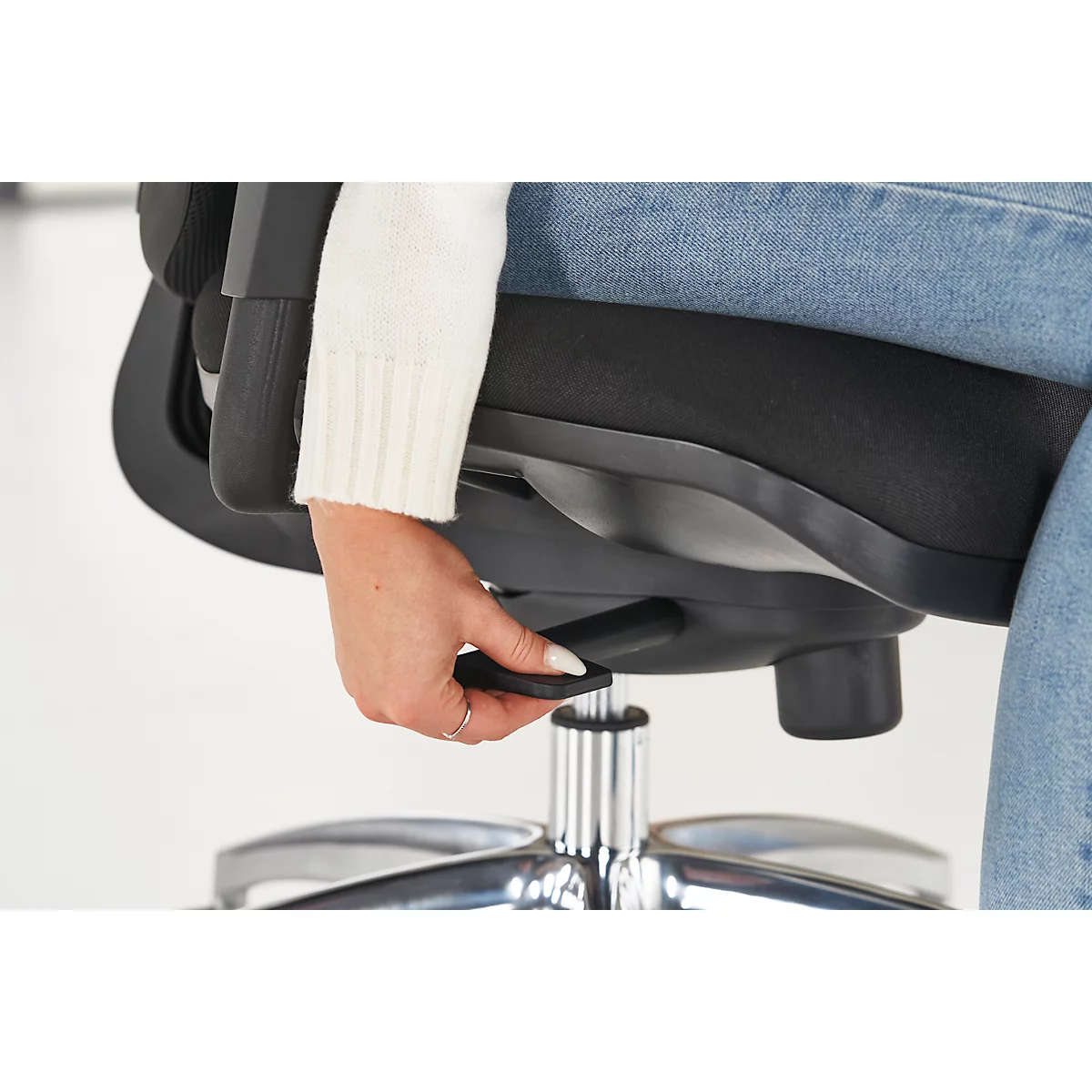 Close-up of a person operating the lever of a black office chair to adjust the height.