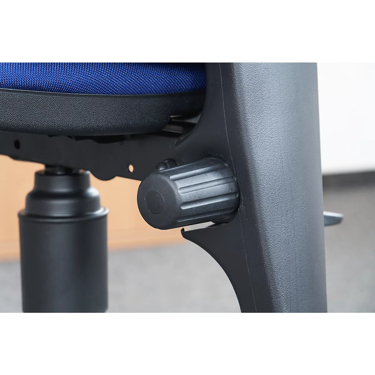 Close-up of a black office chair, detail of the height adjustment. Blue seat cushion in the background.