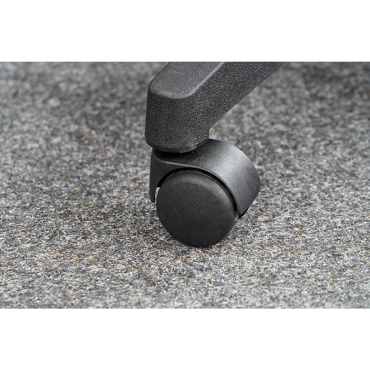 Close-up of a chair wheel standing on gray carpet. The wheel is black and has a round shape.