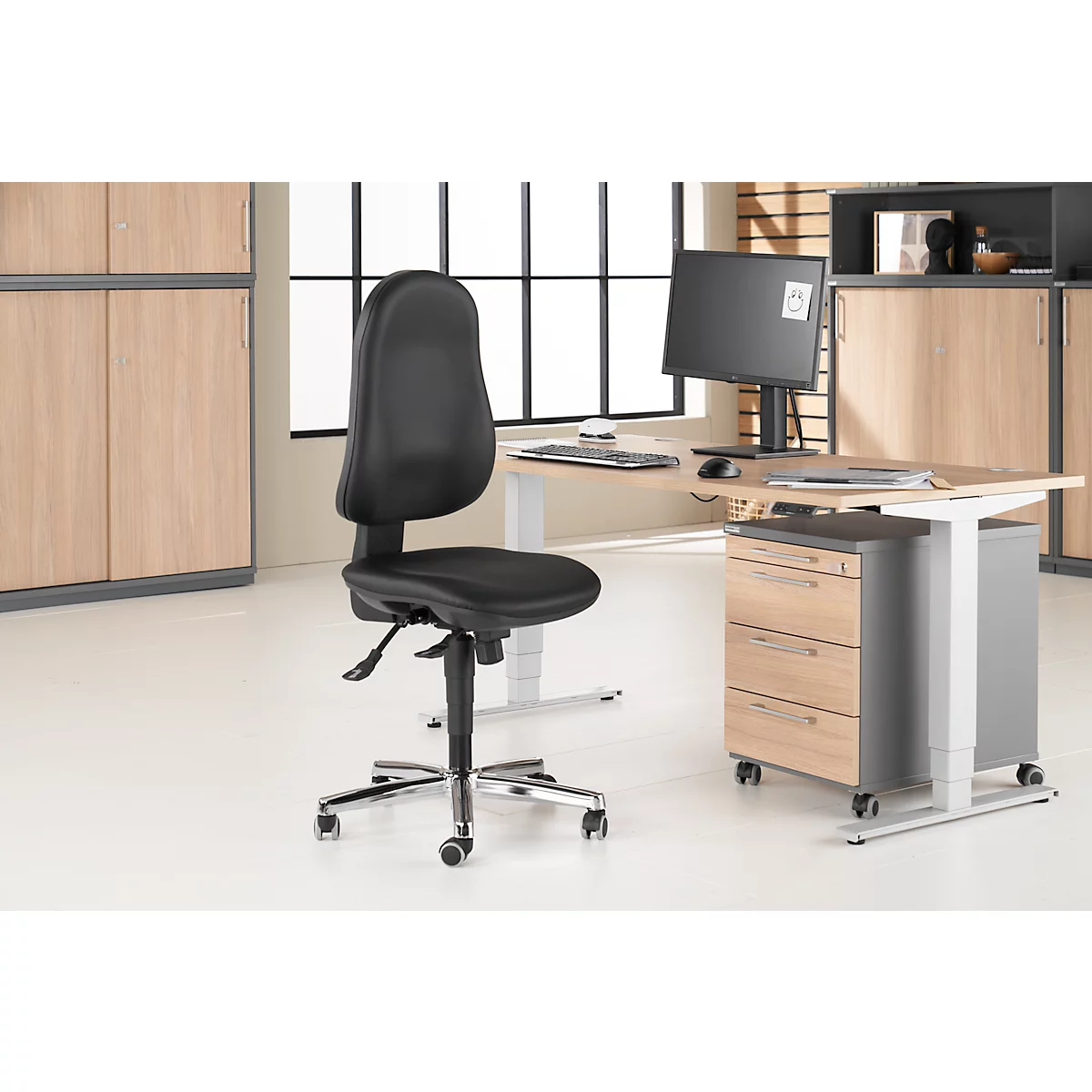 Black office chair in front of light desk with monitor. Background shows cabinets.