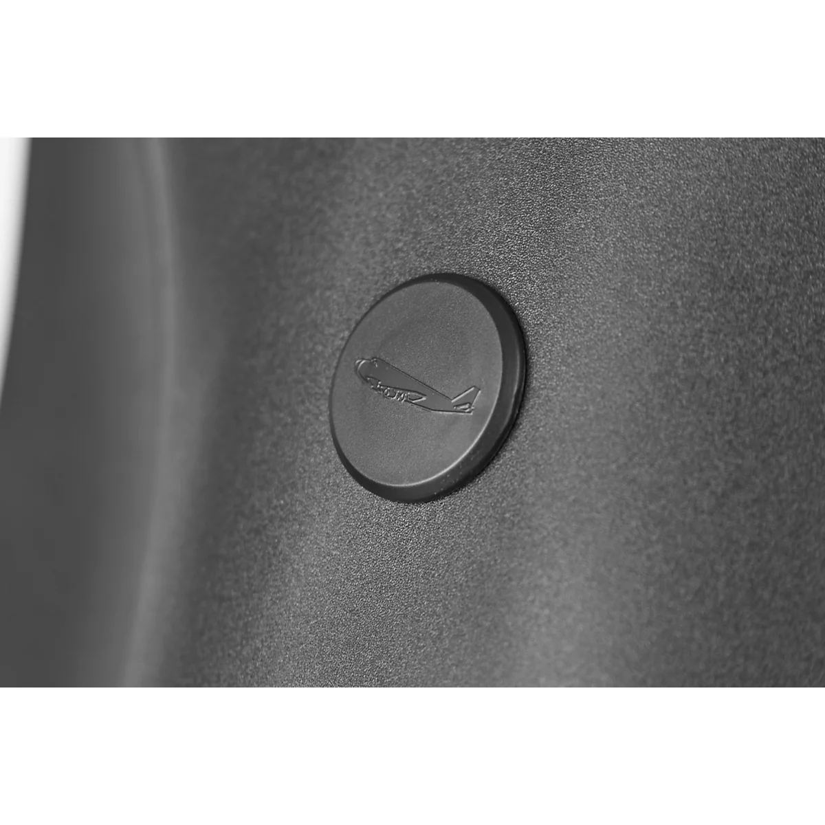 Grayscale image of a round, black button with an airplane motif on a textured surface.