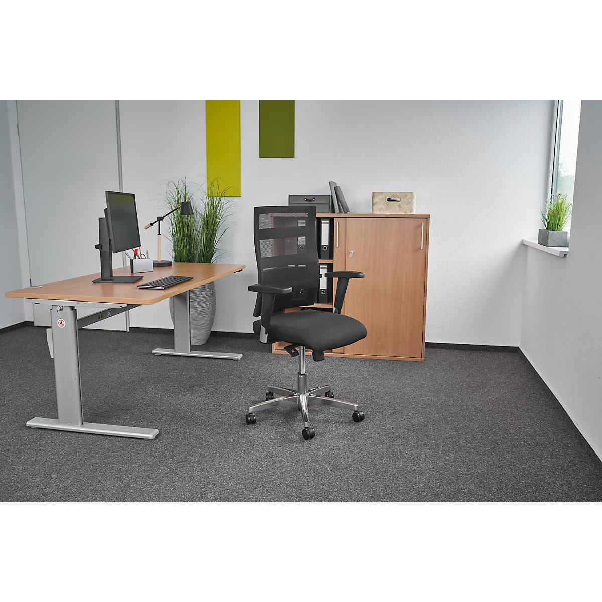 Office chair in an office. The chair is black and is in front of a wooden cabinet.