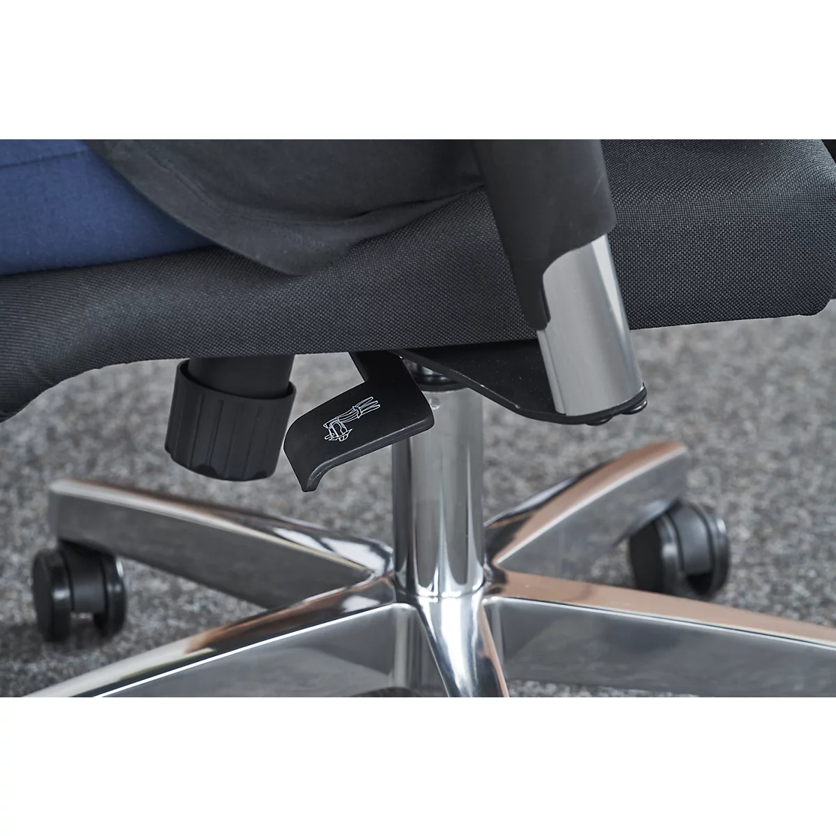 Close-up of chair: lever, chrome frame and fabric seat cover. Part of the person is visible in the picture.