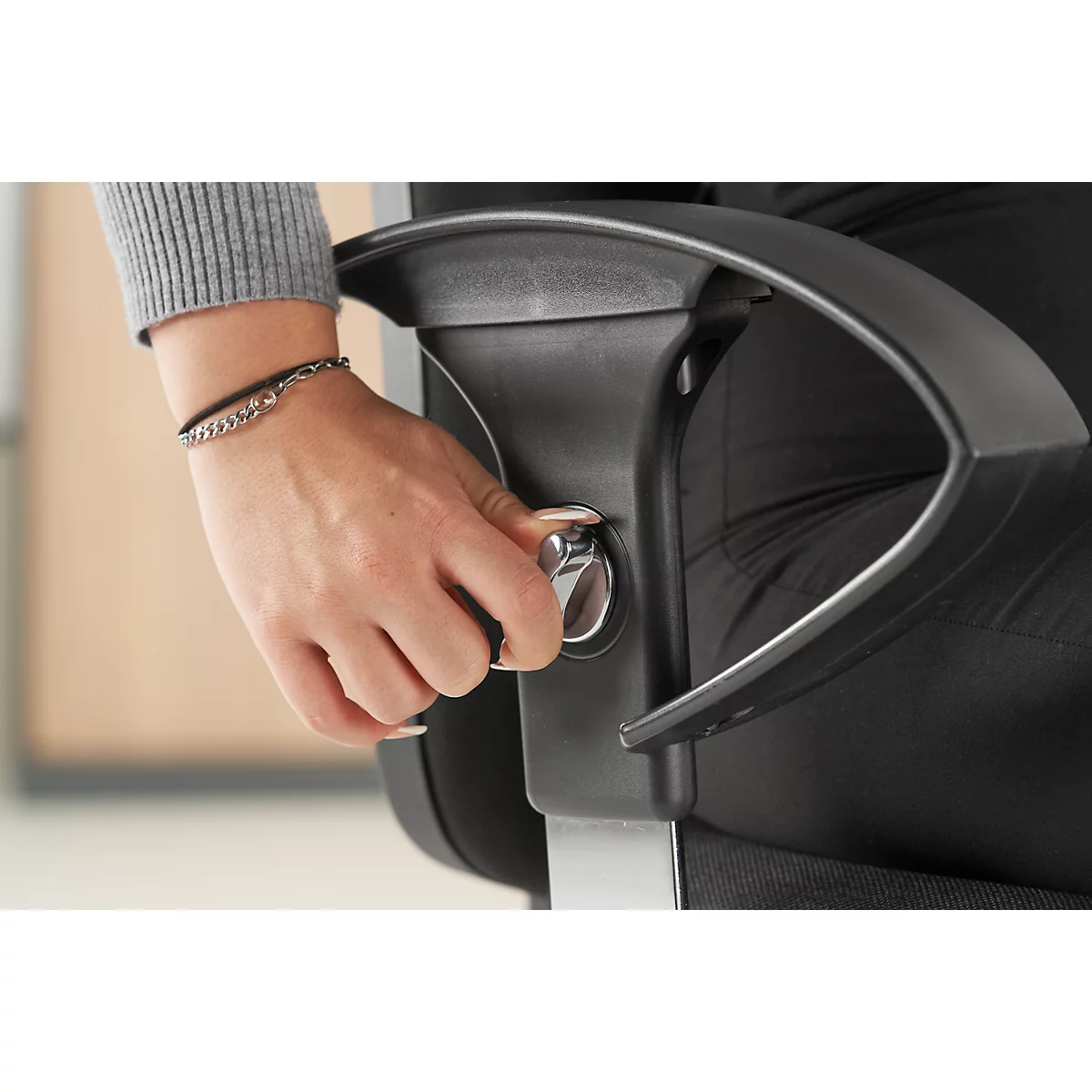 Hand on office chair, turning a silver lever on the armrest.