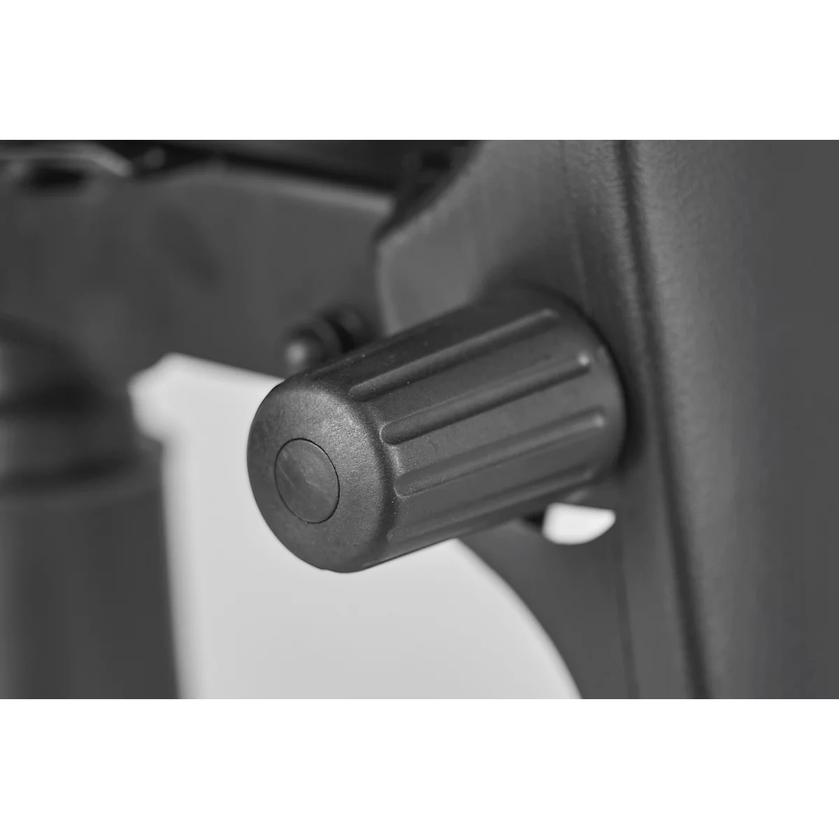 Close-up of a black knob on an office chair. The knob has ribbed sides and a round, slightly recessed center.