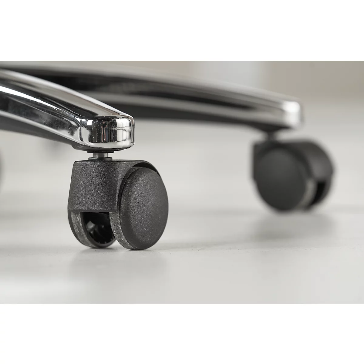 Close-up of black chair casters on a light surface. Chrome struts are visible.